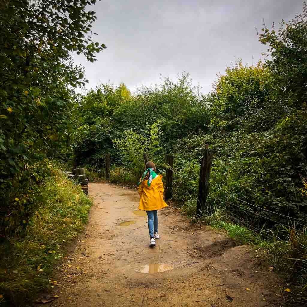 Girl In Yellow Jacket And Jeans Walking Down Muddy Path