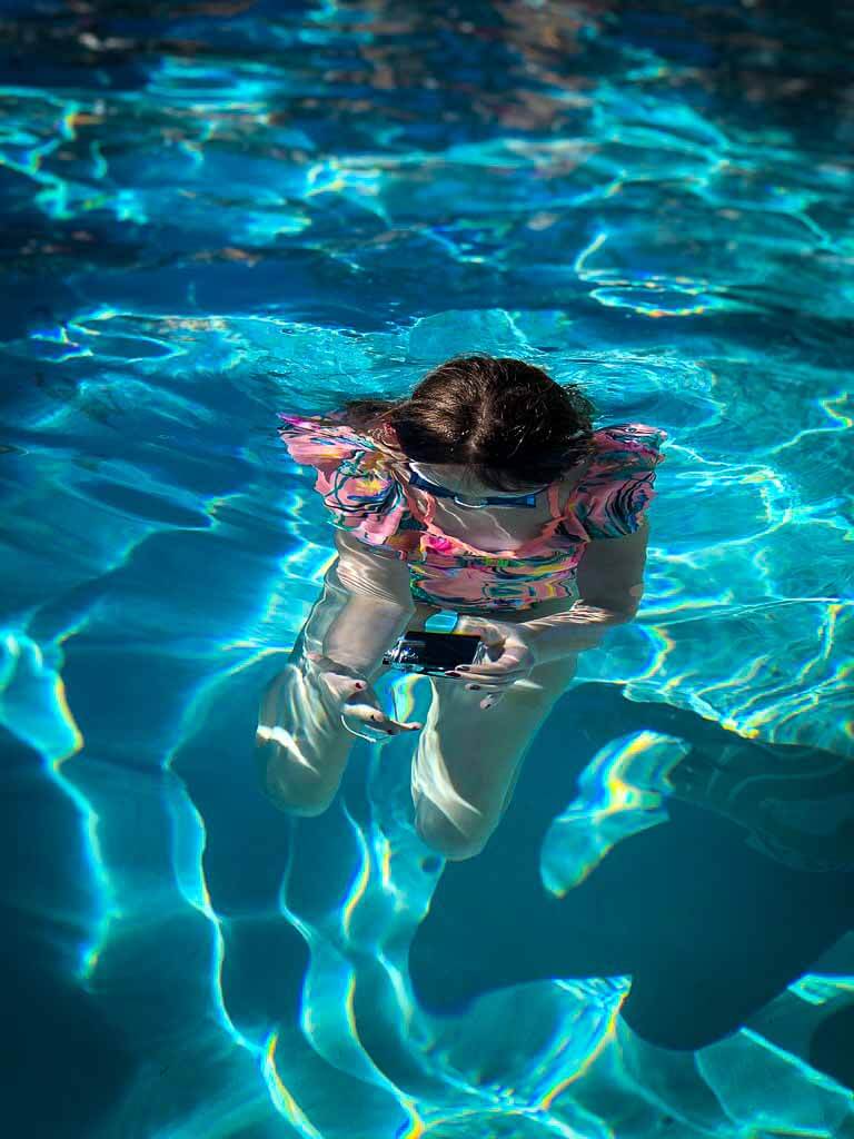 girl in pink swimsuit with goggles underwater taking a photo
