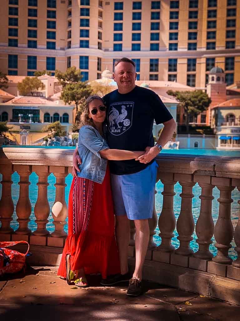 karen quinn in long red dress and denim jacket with arms round nigel quinn in shorts and a t shirt