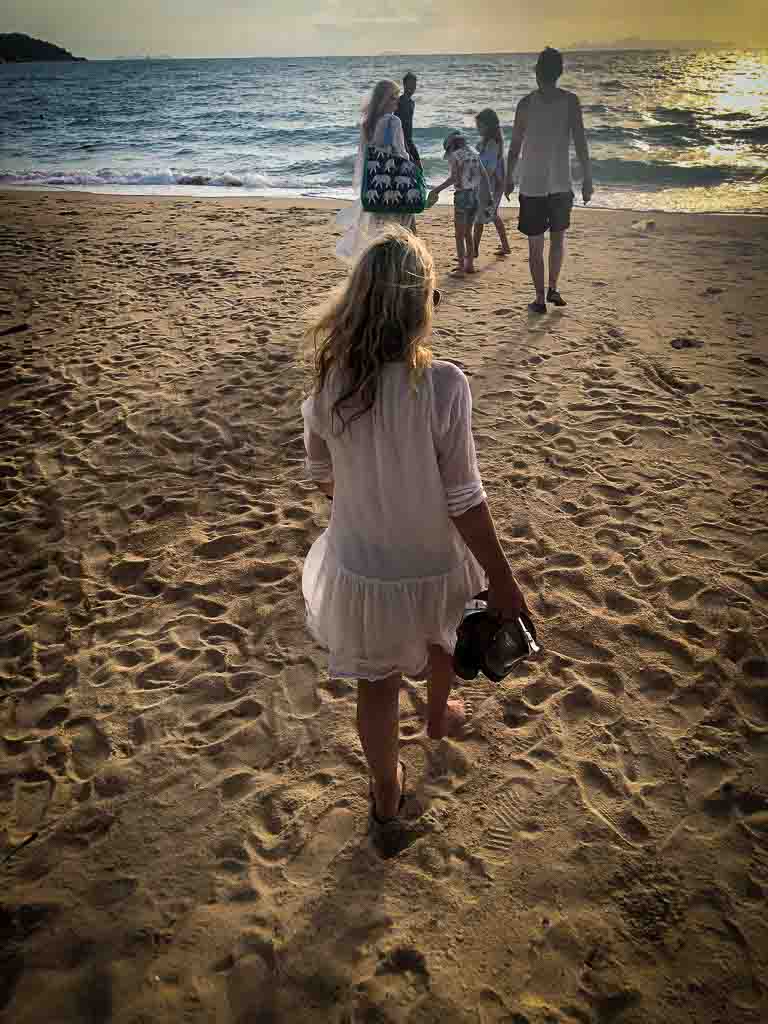 karen quinn with her back to the camera in a white dress walking towards her family at the sea