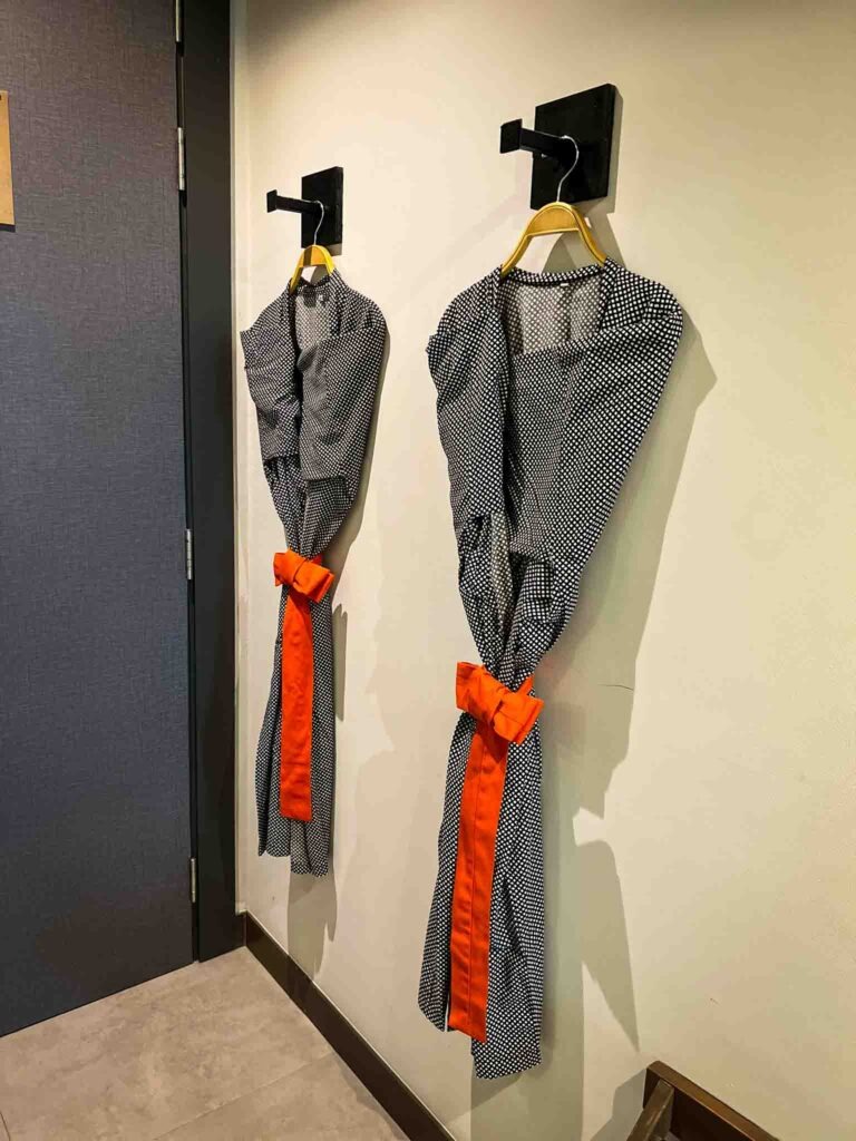 two grey and orange bath robes hanging next to each other on wall hangers
