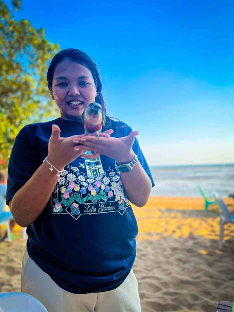 thai woman on a beach holding up a parakeet