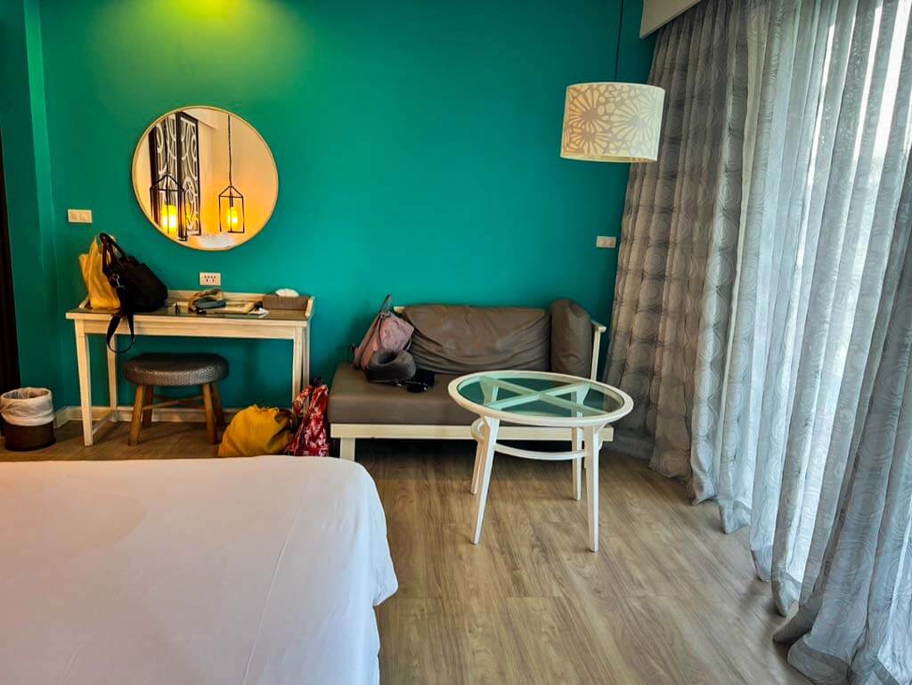 small desk under a round mirror in front of a bright turquiose wall