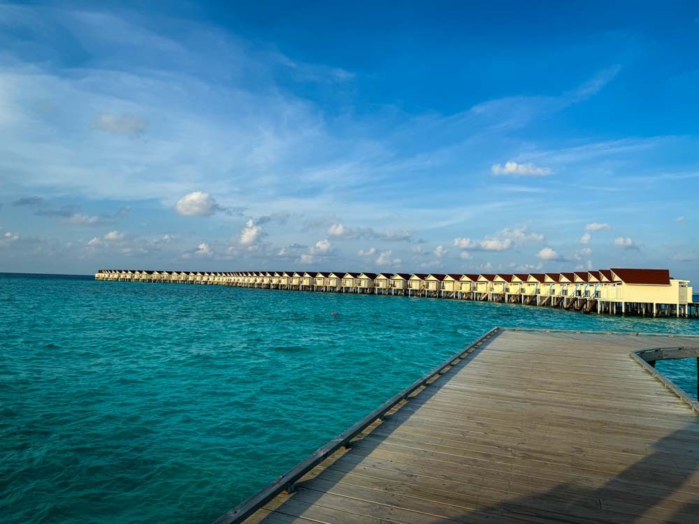 view of the white overwater villas at Oblu xperience ailafushi in the Maldives. Shown from a wooden boardwalk over a bright blue sea